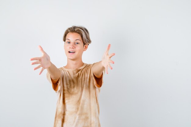 Jonge tienerjongen in t-shirt die armen opent voor knuffel en er vrolijk uitziet, vooraanzicht.