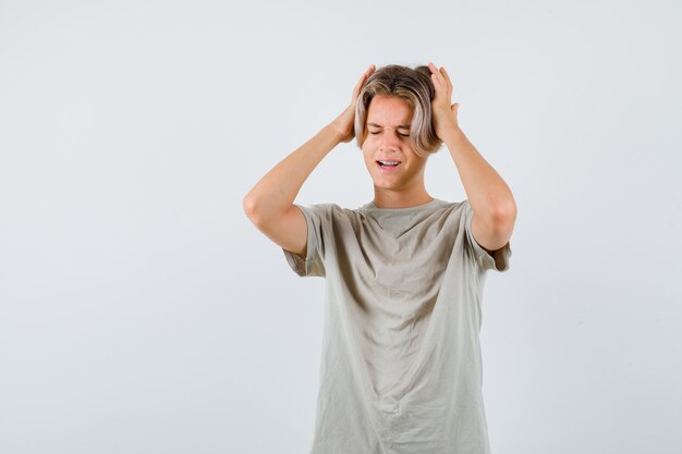 Jonge tienerjongen in t-shirt die handen op het hoofd houdt en neergeslagen kijkt, vooraanzicht.