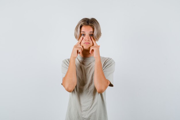 Jonge tienerjongen in t-shirt wijzend naar zijn oogleden en verdrietig kijkend