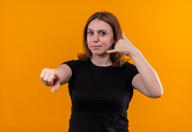 Jonge toevallige vrouw die vraaggebaar doet en en op geïsoleerde oranje muur richt kijkt