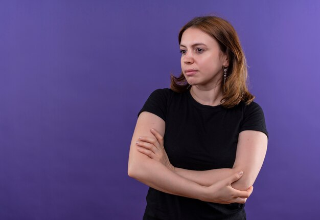 Jonge toevallige vrouw die zich met gesloten houding bevindt en naar linkerkant op geïsoleerde purpere muur met exemplaarruimte kijkt