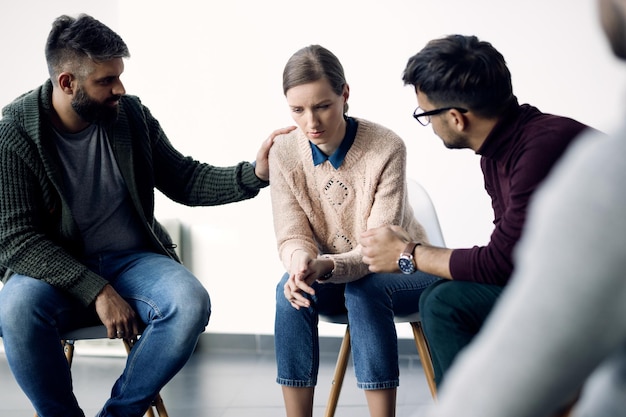 Jonge trieste vrouw wordt getroost tijdens groepstherapiebegeleiding