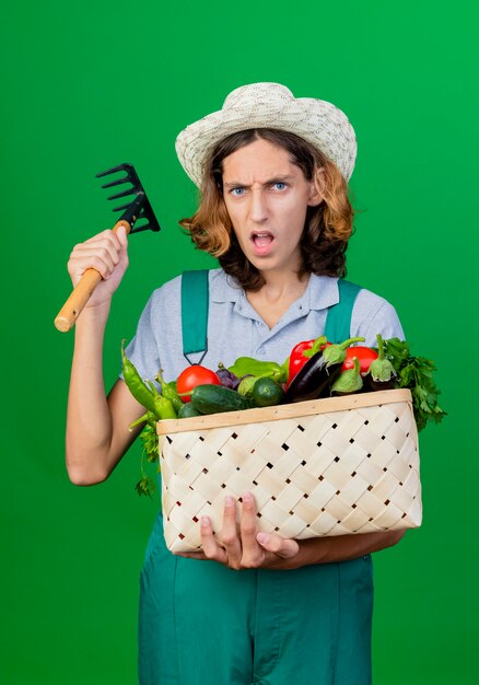Jonge tuinman man dragen jumpsuit en hoed bedrijf krat vol verse groenten