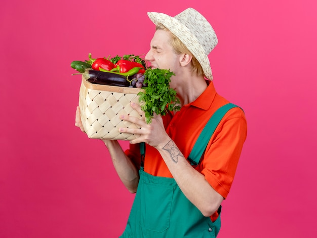 Jonge tuinman man met jumpsuit en hoed bedrijf krat vol groenten