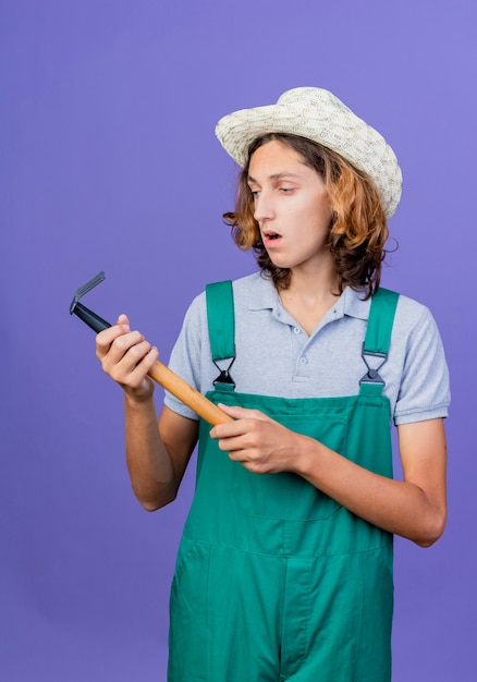 Jonge tuinman man met jumpsuit en hoed met mini hark te kijken naar het wordt verward