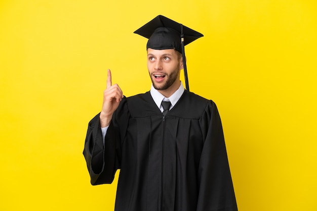 Jonge, universitair afgestudeerde blanke man geïsoleerd op gele achtergrond die omhoog wijst en verrast Premium Foto