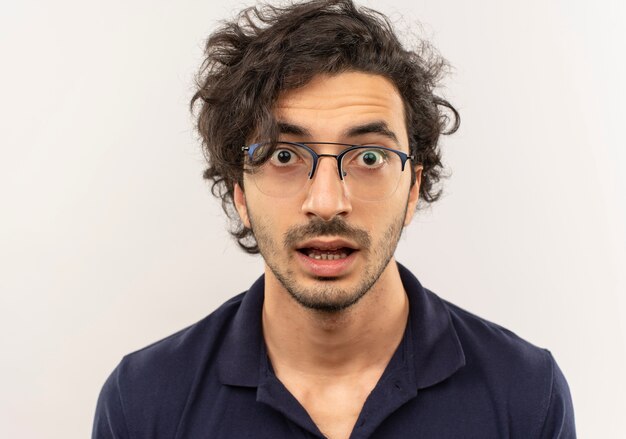 Jonge verbaasde man in zwart shirt met optische bril kijkt geïsoleerd op een witte muur