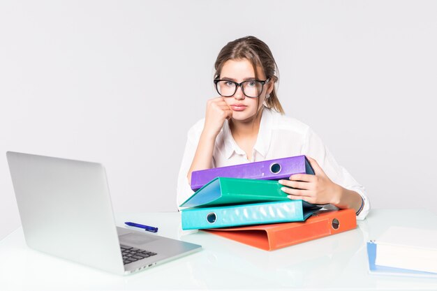 Jonge vermoeide bedrijfsdievrouw met omslagen op bureau op witte achtergrond wordt geïsoleerd