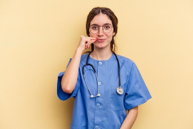 Jonge verpleegster blanke vrouw geïsoleerd op gele achtergrond met vingers op lippen houden een geheim.