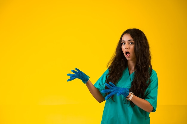 Jonge verpleegster in groene uniforme en plastic handschoenen die verbaasd gezicht maken