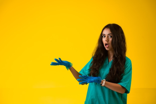 Jonge verpleegster in groene uniforme en plastic handschoenen die verrast gezicht maken.