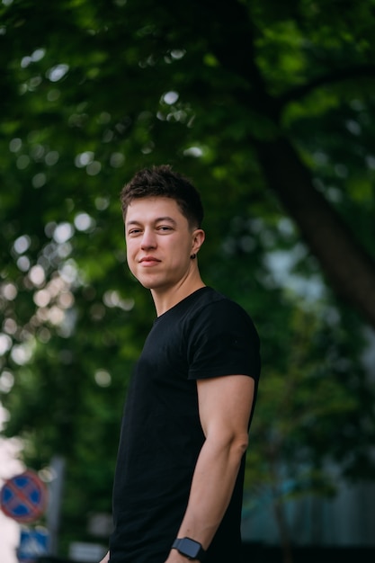 Jonge volwassen man in een zwart t-shirt en spijkerbroek loopt op een straat in de stad