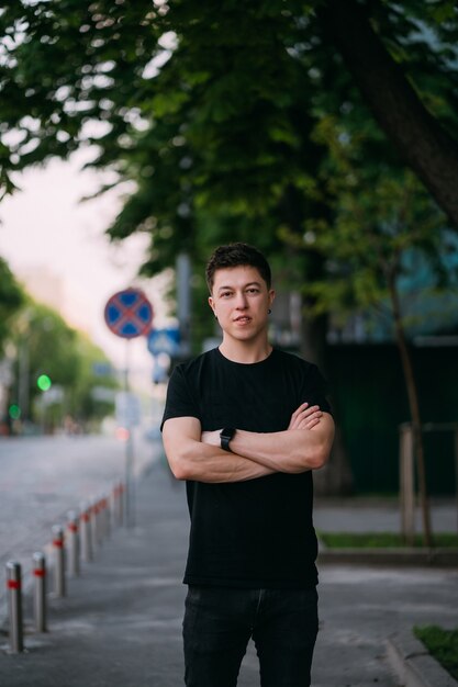 Jonge volwassen man in een zwart t-shirt en spijkerbroek loopt op een straat in de stad