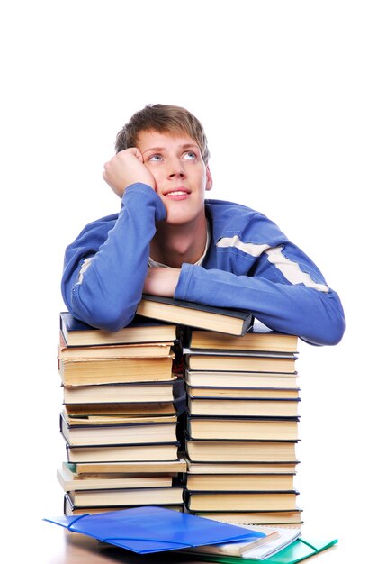 Jonge volwassen student die op hoop van de boeken wordt bijgehouden die omhoog kijkt en denkt.