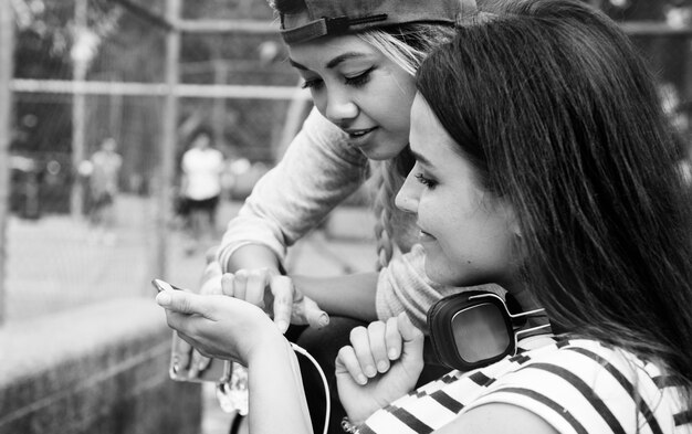 Jonge volwassen vrouwelijke vrienden luisteren naar muziek via hun smartphone buitenshuis