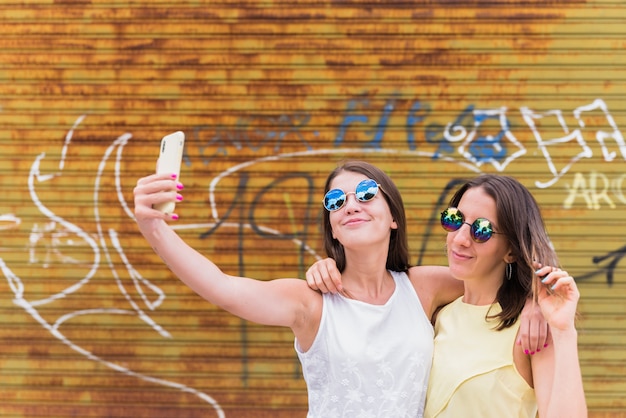 Jonge vriendinnen die selfie tegen graffitimuur maken