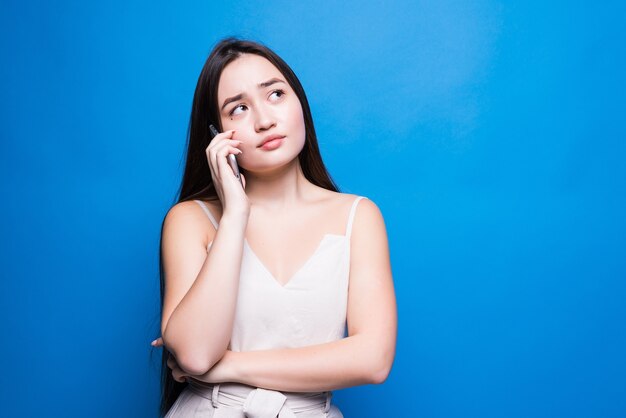Jonge vrij Aziatische vrouw die op mobiele telefoon spreekt die over blauwe muur wordt geïsoleerd