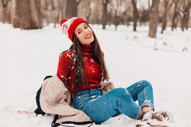 Jonge vrij lachende gelukkige vrouw in rode wanten en gebreide muts dragen winterjas, wandelen in het park, spelen met sneeuw in warme kleren