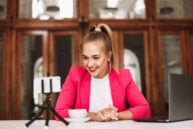 Jonge vrolijke blogger in roze jasje neemt graag nieuwe video op voor haar vlog