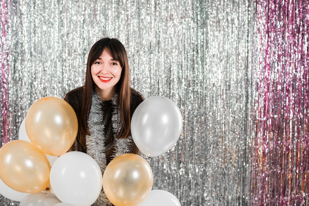 Jonge vrolijke dame die vele ballonnen in de buurt van klatergoud