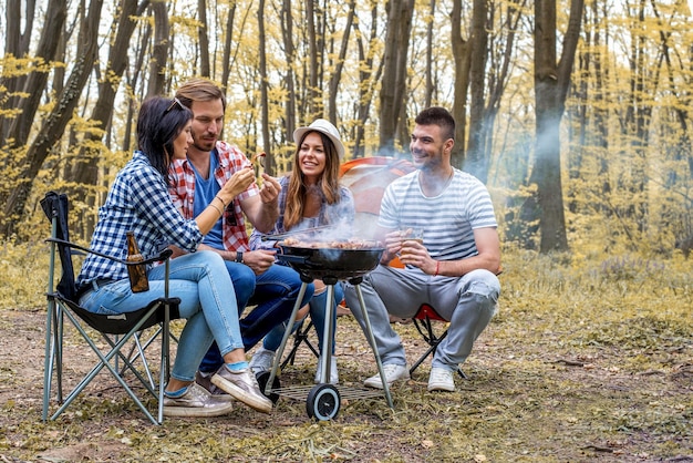 Jonge vrolijke vrienden die barbecue buitenshuis voorbereiden