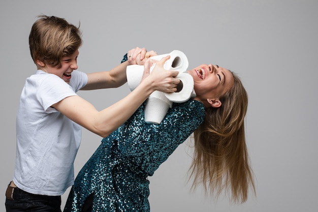 Jonge vrolijke vrouw vecht voor veel wc-papier met een jonge jongen, portret geïsoleerd op een witte achtergrond