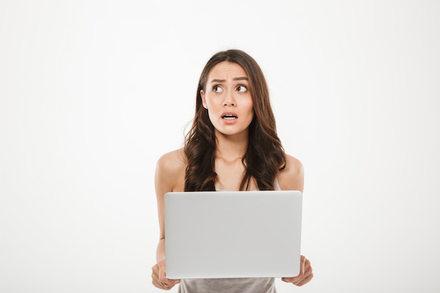 jonge vrouw 30s wegkijken wordt benadrukt of teleurgesteld tijdens het gebruik van zilveren notebook in de hand, geïsoleerd over witte muur