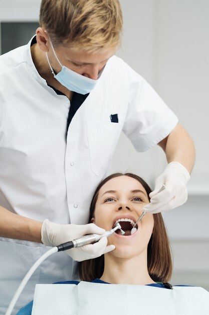 Jonge vrouw aan de tandartsstoel tijdens een tandheelkundige schalingsprocedure