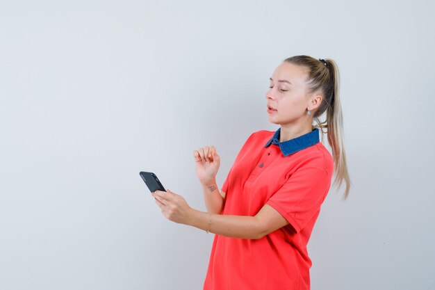 Jonge vrouw aandachtig kijken naar mobiele telefoon in t-shirt, vooraanzicht.