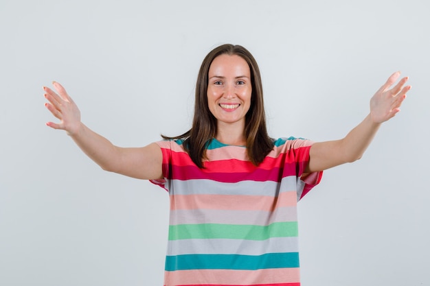 Jonge vrouw armen wijd openen in t-shirt en op zoek vrolijk, vooraanzicht.