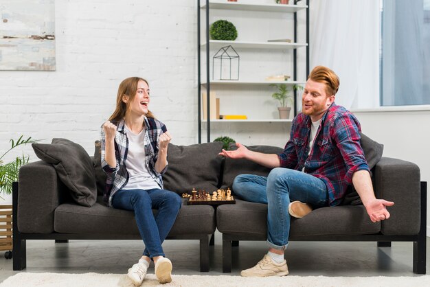 Jonge vrouw balde haar vuist met vreugde kijken naar zijn vriend schouderophalend tijdens het spelen van het schaak