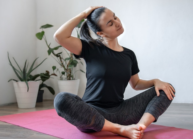 Jonge vrouw beoefent asana's thuis op de mat, yoga thuis, de spieren van het lichaam strekkend.