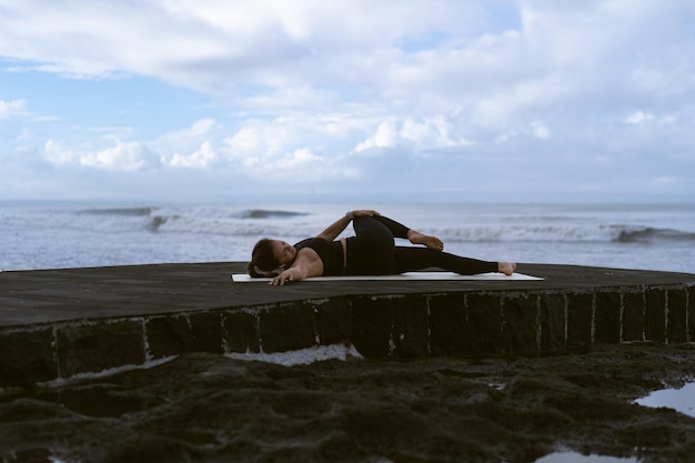 Jonge vrouw beoefent yoga op een prachtig strand bij zonsopgang. Blauwe lucht, oceaan, golven, nabijheid van de natuur, eenheid met de natuur.