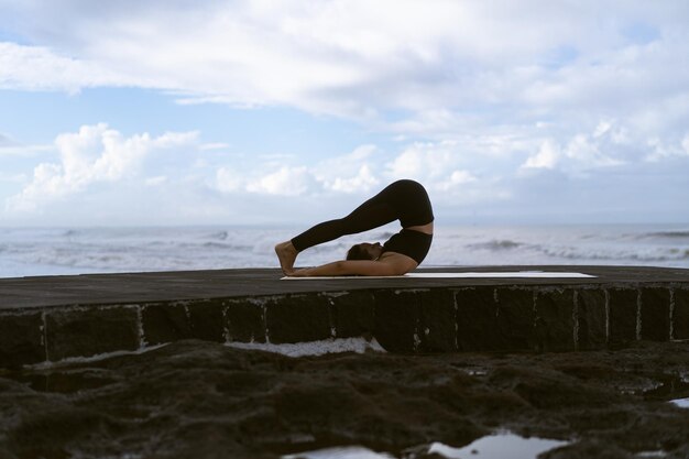 Jonge vrouw beoefent yoga op een prachtig strand bij zonsopgang. Blauwe lucht, oceaan, golven, nabijheid van de natuur, eenheid met de natuur.
