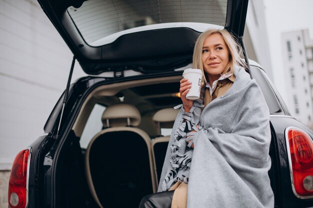 Jonge vrouw bij haar auto staan en koffie drinken