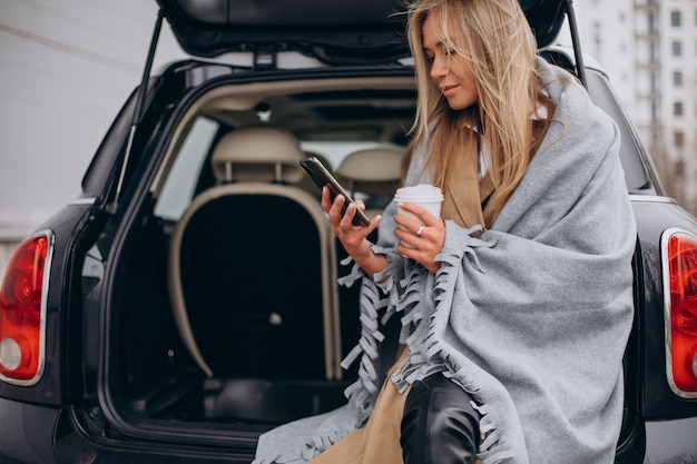 Jonge vrouw bij haar auto staan en koffie drinken