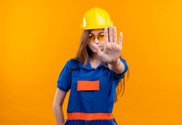 Jonge vrouw bouwer werknemer in de bouw uniform en veiligheidshelm permanent met open hand stopbord maken