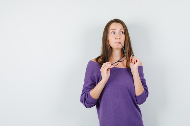 Jonge vrouw bril in violet overhemd bijten en aarzelend, vooraanzicht op zoek.