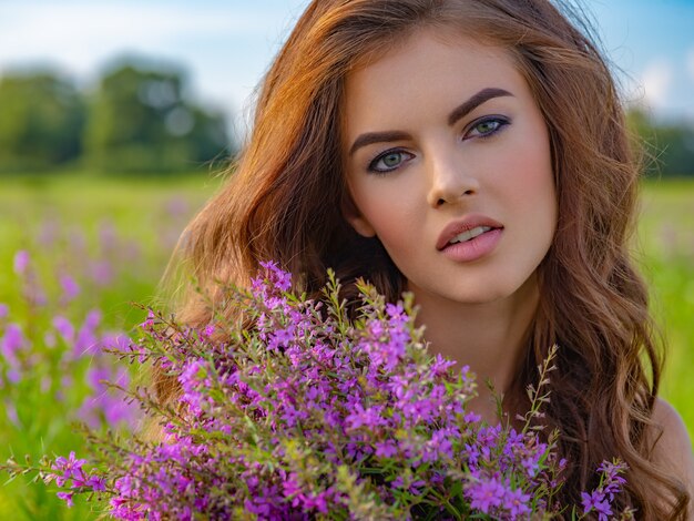 Jonge vrouw buitenshuis met een boeket. Meisje in een veld met lavendelbloemen in haar handen. Close-upportret van een Kaukasische vrouw op aard.