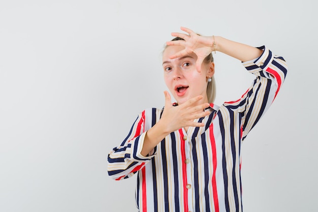 Jonge vrouw camera handgebaar in gestreepte blouse tonen en gelukkig kijken