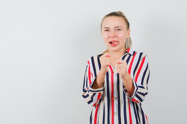 Gratis foto jonge vrouw camera handgebaar in gestreepte blouse tonen en optimistisch op zoek