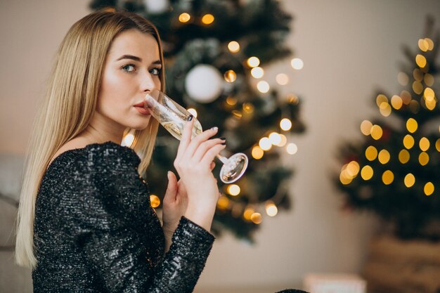 Jonge vrouw champagne drinken door kerstboom