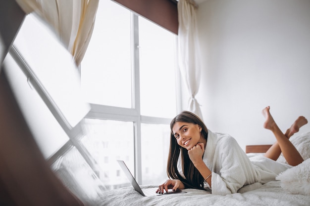 Jonge vrouw die aan computer in bed werkt