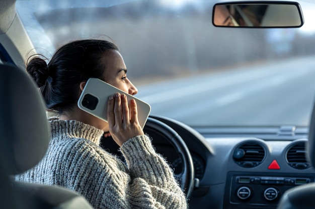 Jonge vrouw die aan de telefoon praat tijdens het autorijden