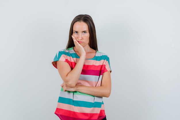 Jonge vrouw die aan kiespijn in t-shirt lijdt en somber kijkt. vooraanzicht.