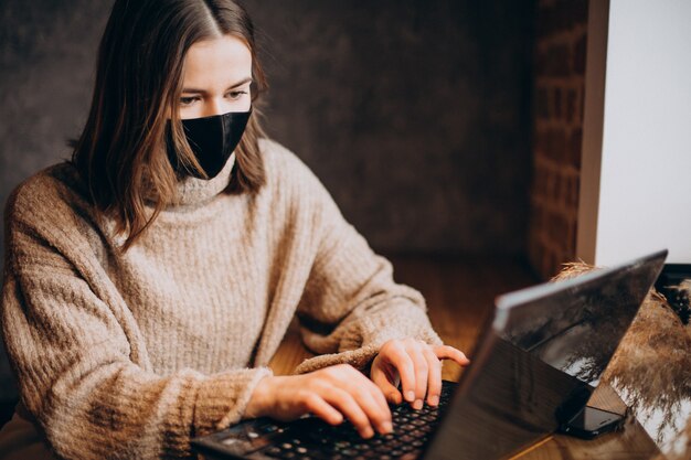 Jonge vrouw die aan laptop in een koffie werkt die masker draagt