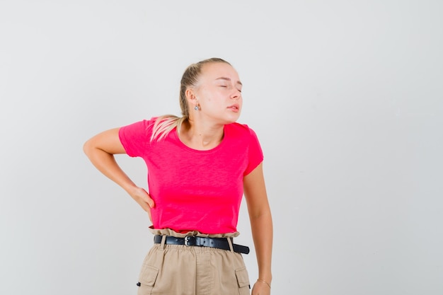 Jonge vrouw die aan rugpijn in t-shirt en broek lijdt en uitgeput kijkt