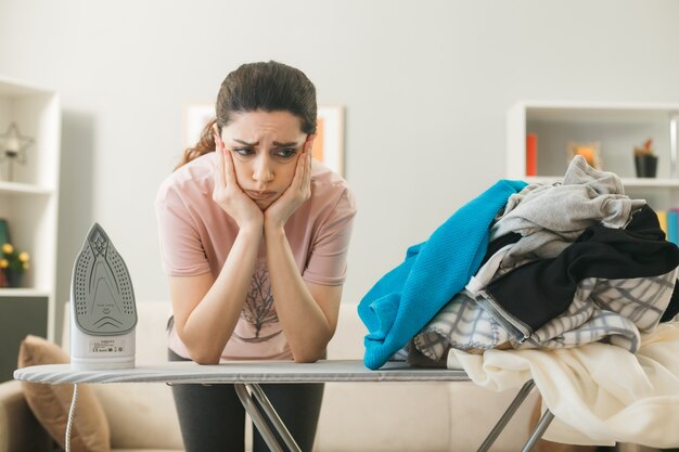 Gratis foto jonge vrouw die achter de strijkplank staat met kleren in de woonkamer