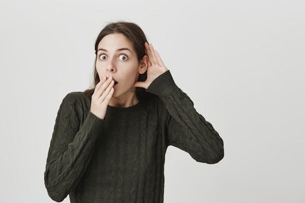 Jonge vrouw die afluistert, hijgend als ze schokkende roddels hoort