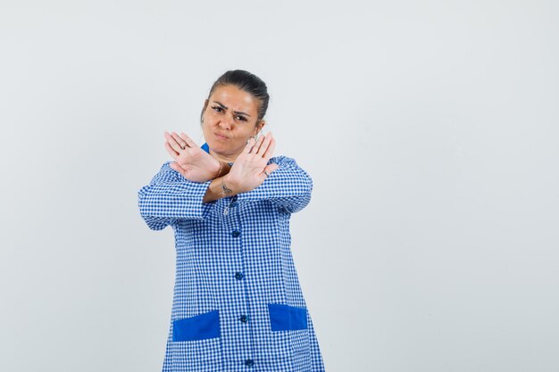 Jonge vrouw die beperking gebaar in het blauwe overhemd van de gingangpyjama toont en boos kijkt. vooraanzicht.